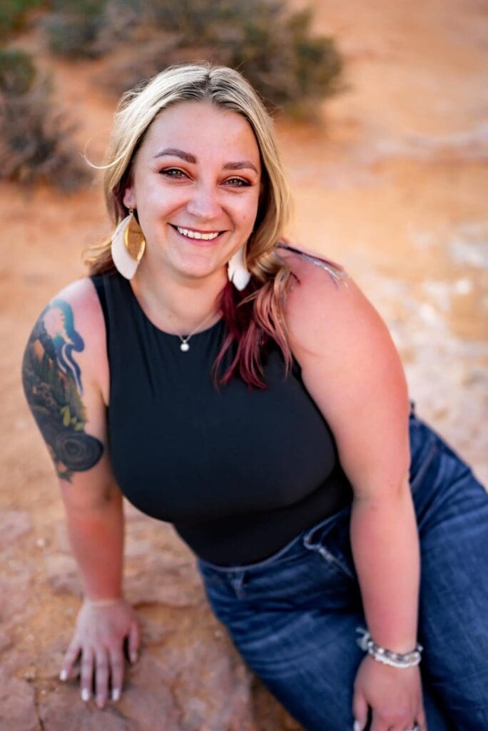 Photographer posing outdoors at Arches National Park, sitting against an orange-hued rock background in casual attire.