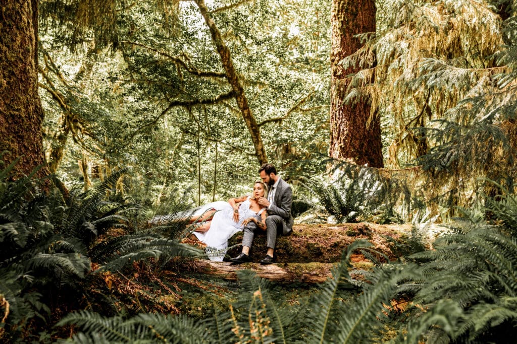 Elopement couple laying on the forest floor, surrounded by moss-covered trees in Olympic National Park.