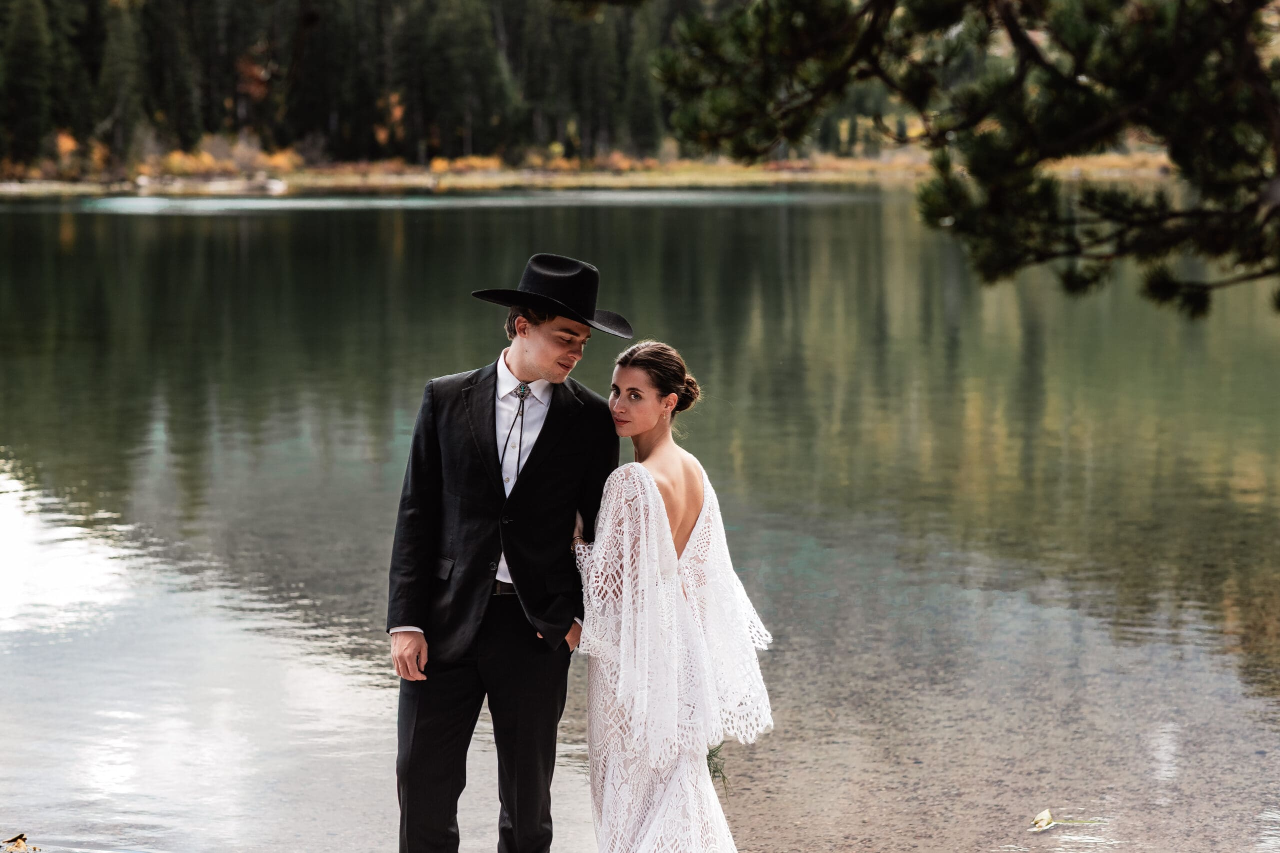 Bride and groom walking along a serene lakeside path at String Lake, surrounded by autumn foliage and mountain views in Grand Teton National Park.