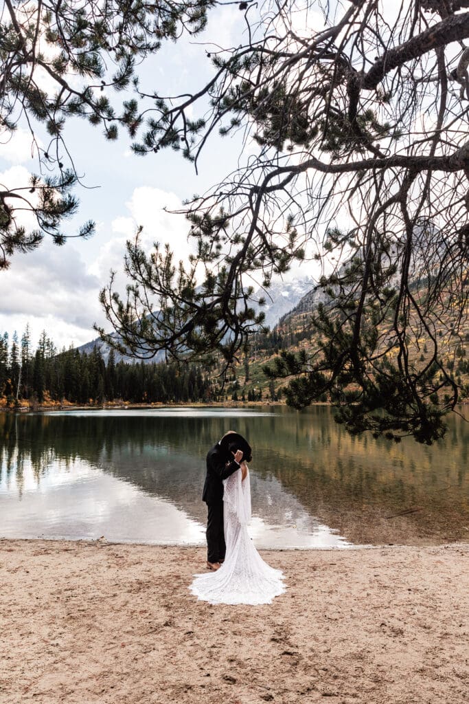 Couple embracing beside String Lake surrounded by autumn foliage and rugged mountain peaks in Grand Teton National Park.