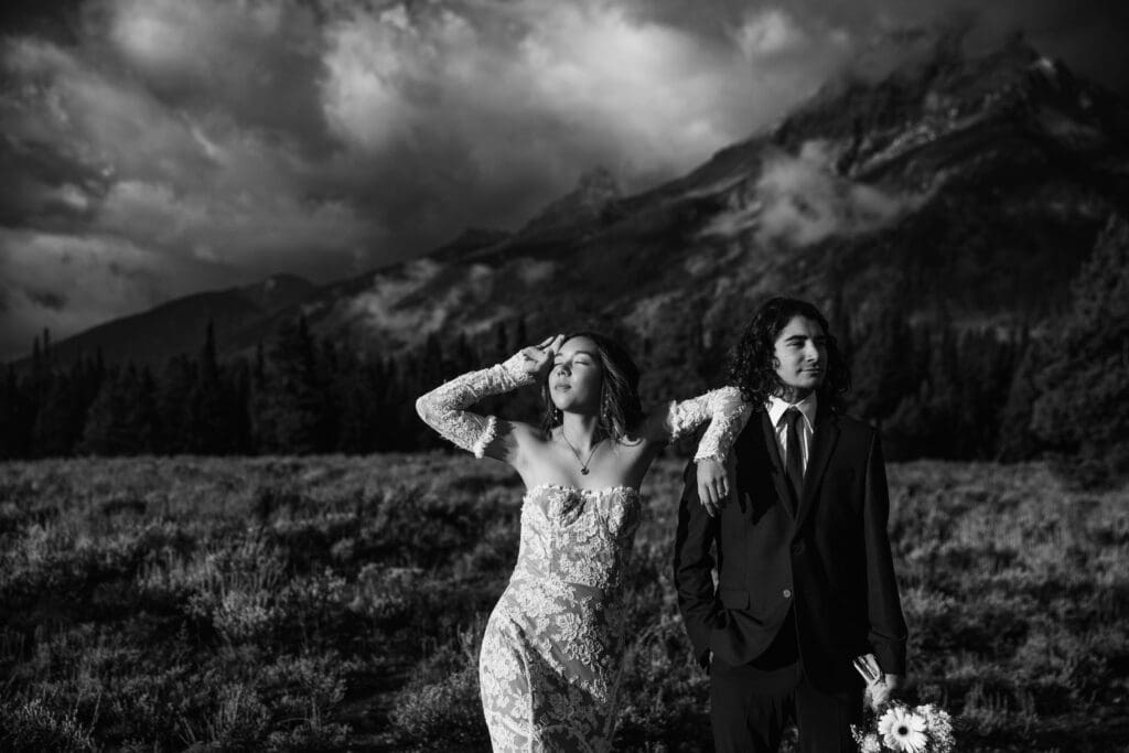 Black and white editorial elopement portrait of a couple posed at Cascade Canyon Turnout with the Grand Teton mountains rising dramatically behind them.