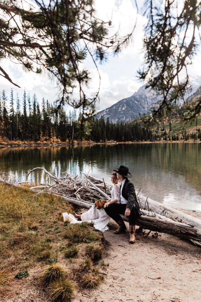 Couple sitting together on a fallen log by String Lake with pine trees and the Grand Teton mountains in the background.