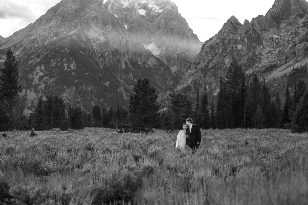 Editorial black and white portrait of an elopement couple standing together in a meadow with snow-capped Grand Teton peaks in the background.