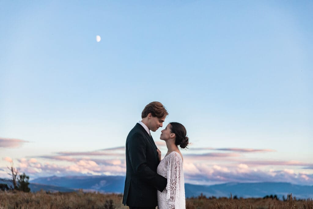 : Bride and groom in wedding attire sharing an intimate embrace against the dramatic mountain backdrop at sunset in Grand Teton National Park.