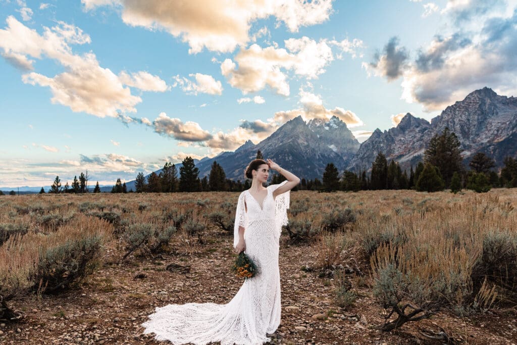 Bride standing alone in a white dress at Mountain View Turnout with the Grand Teton mountains glowing at sunset in Grand Teton National Park.