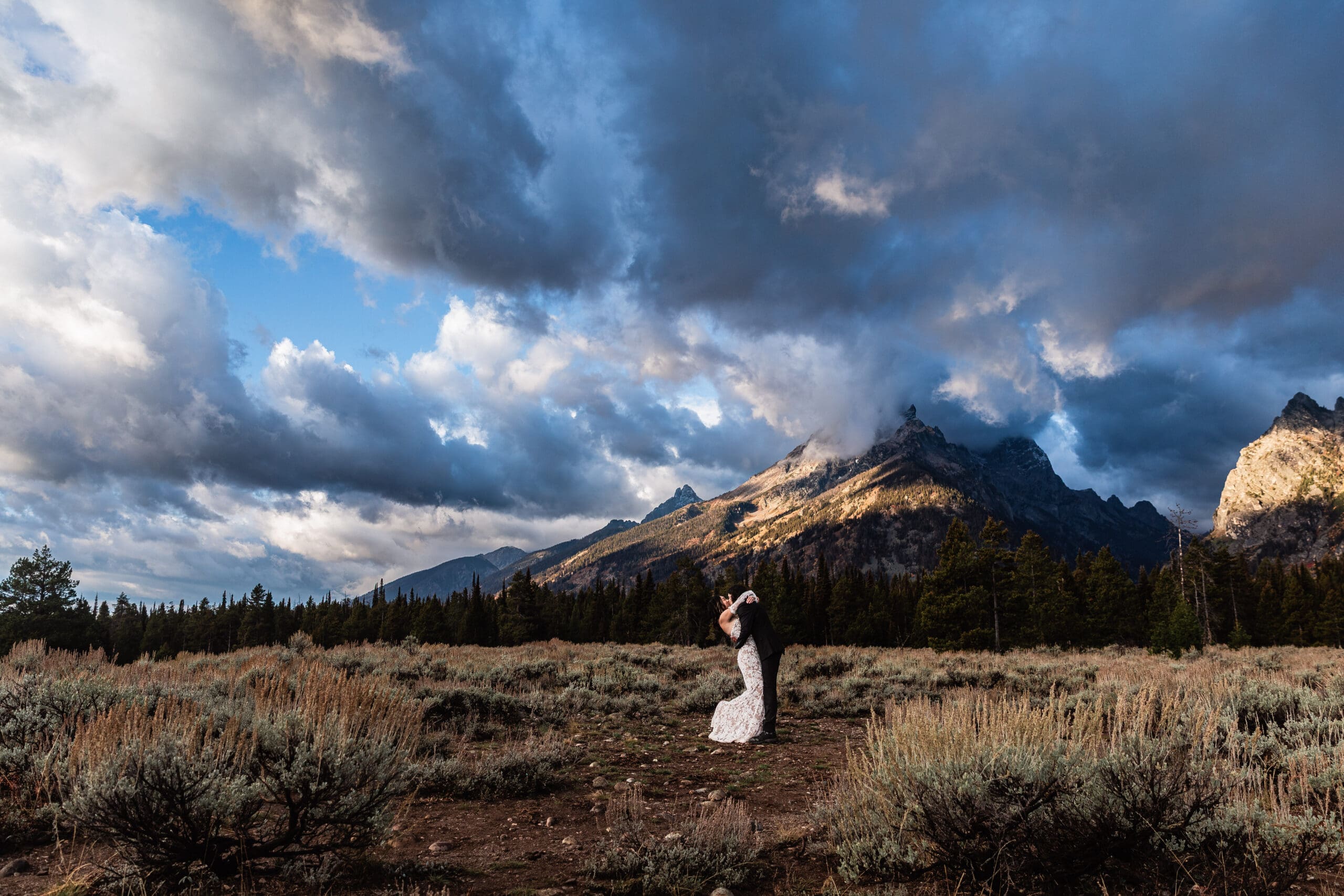 Elopement couple sharing their first kiss at sunset with snow-capped Grand Teton mountains reflected in the calm Snake River.