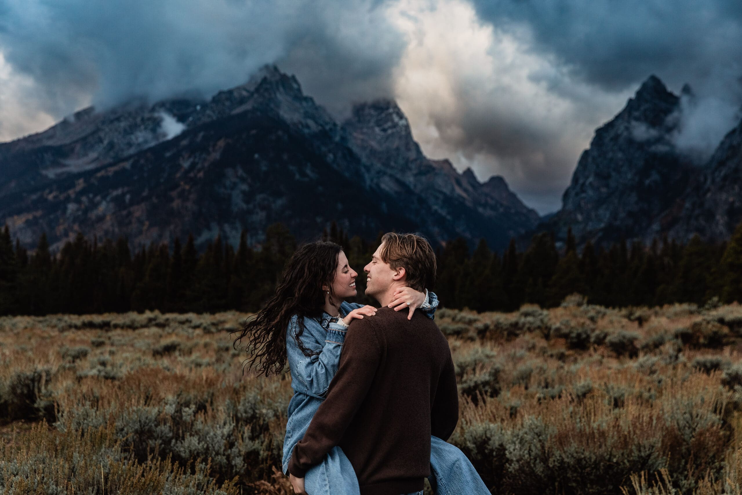Engagement couple sharing a romantic moment at dusk with snow-capped Grand Teton mountains in the background at Grand Teton National Park.