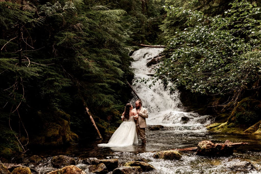 Bride and groom captured in a romantic pose near a forest waterfall at Grove of the Patriarchs, Mount Rainier National Park.