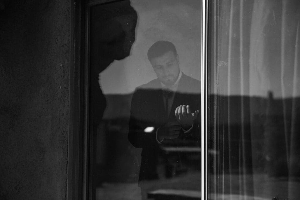 Groom preparing for his elopement inside the Cave Airbnb in Moab, photographed through the window with soft desert light and a quiet, candid feel.