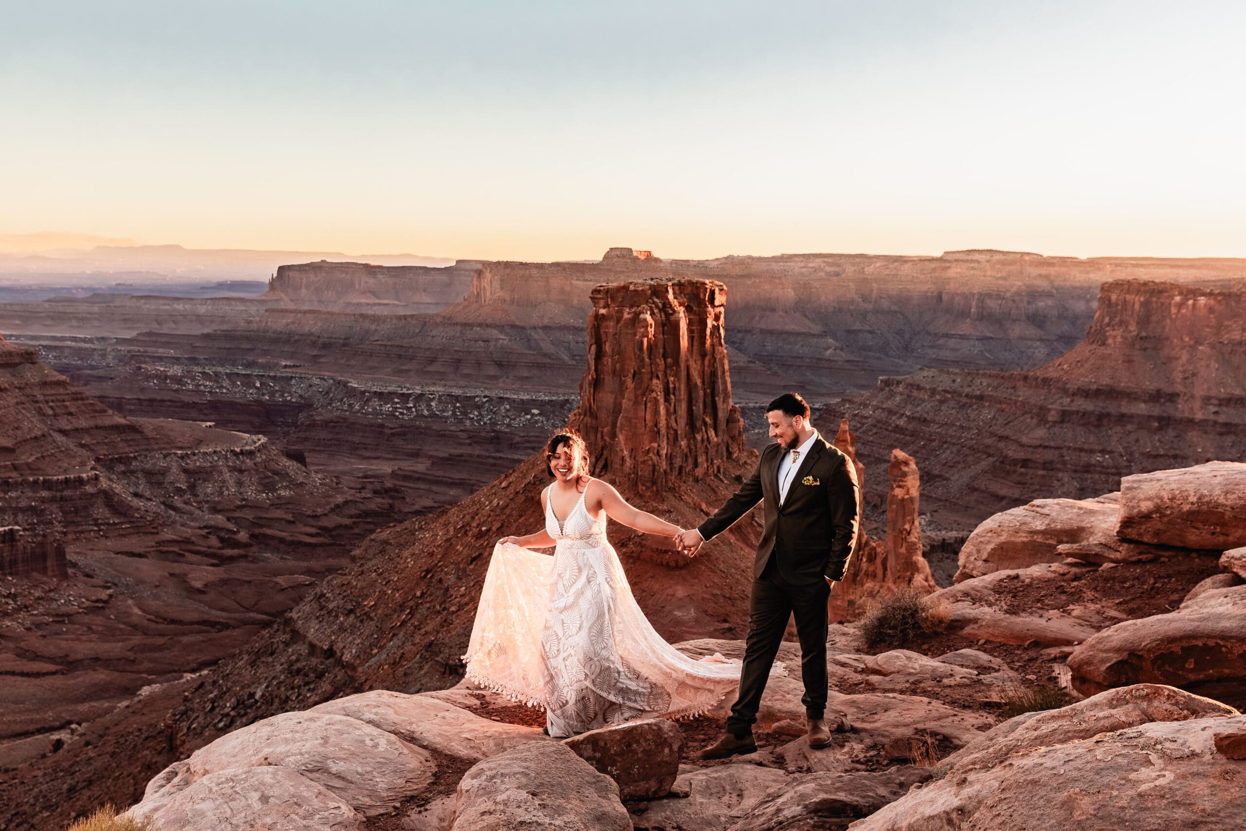 Elopement couple walking together along the cliffside at Marlboro Point in Moab, Utah at sunset, surrounded by red rock desert scenery.