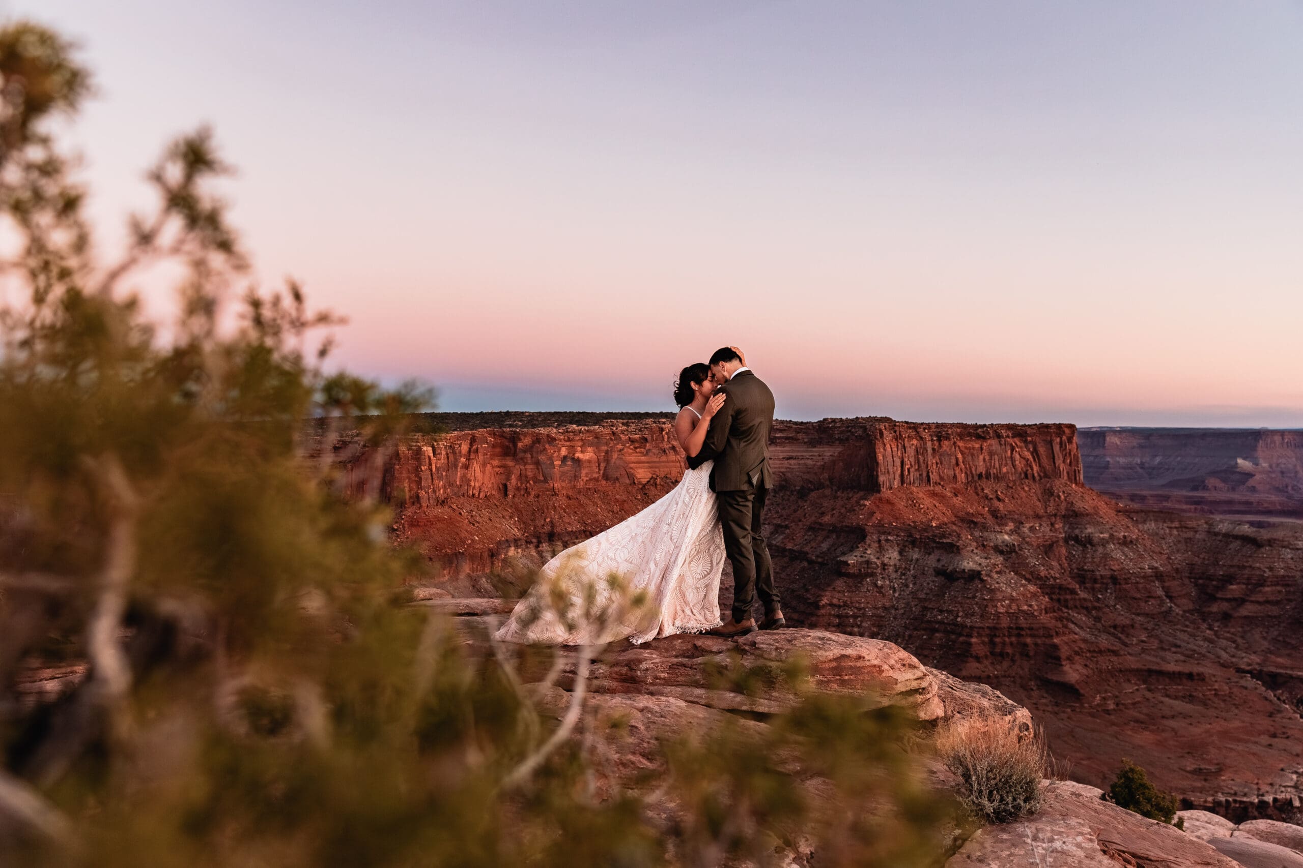 Bride and groom kissing, framed by a juniper tree during their Malboro Point elopement portraits in Moab.