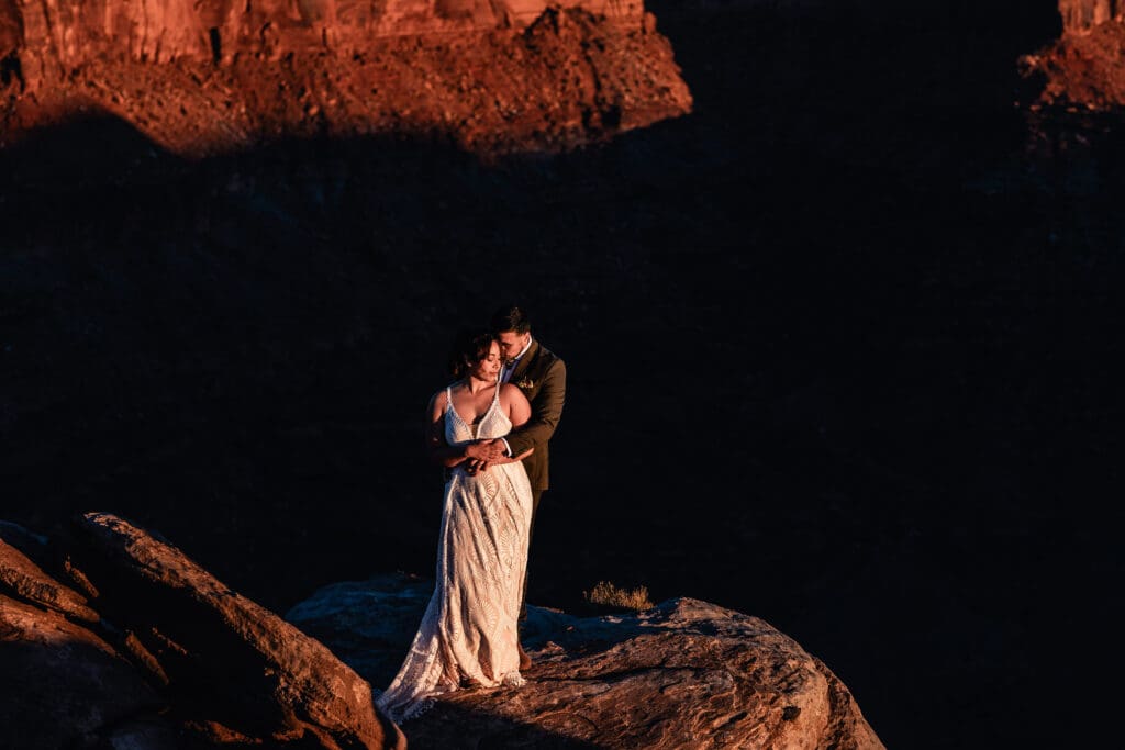 Dramatic overhead shot of groom hugging bride from behind with shadows cast along the rocks at Malboro Point, Moab.