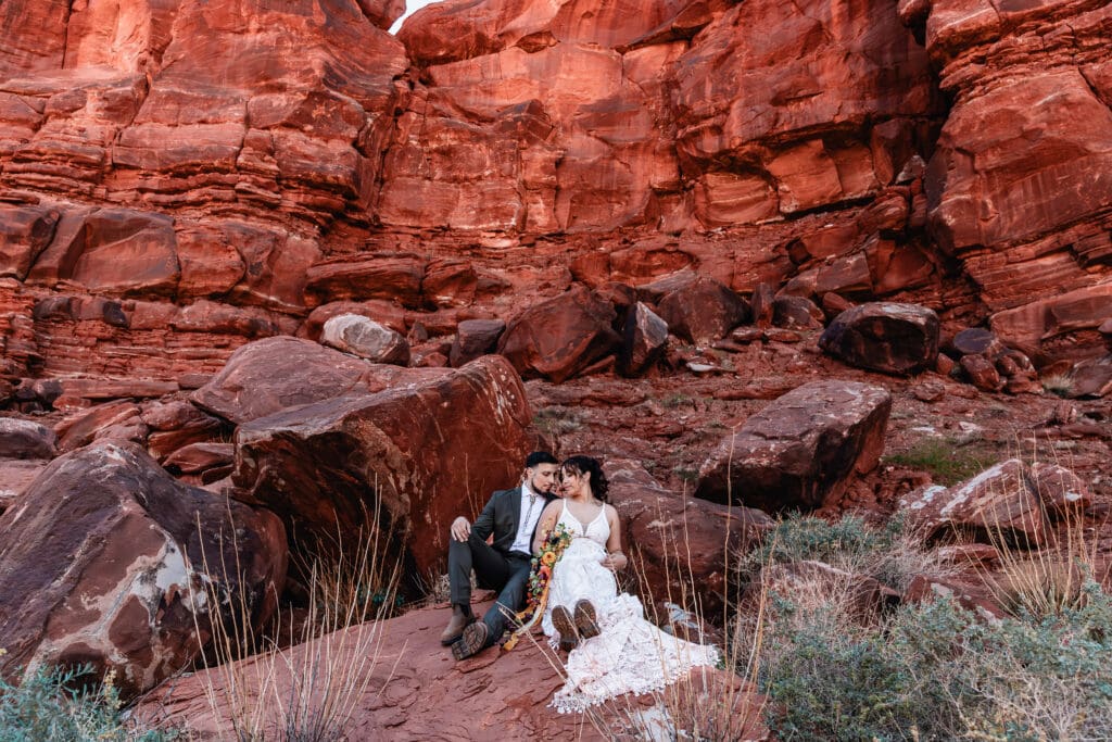 Elopement couple sitting together on red rocks in Moab, Utah, sharing an intimate, quiet moment during their desert adventure.