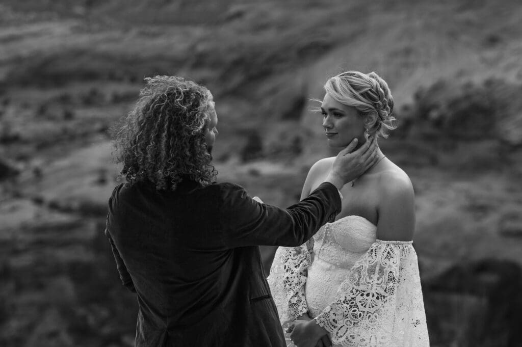 Black and white portrait capturing the couple’s quiet, emotional moment exchanging vows beneath Corona Arch in Moab.