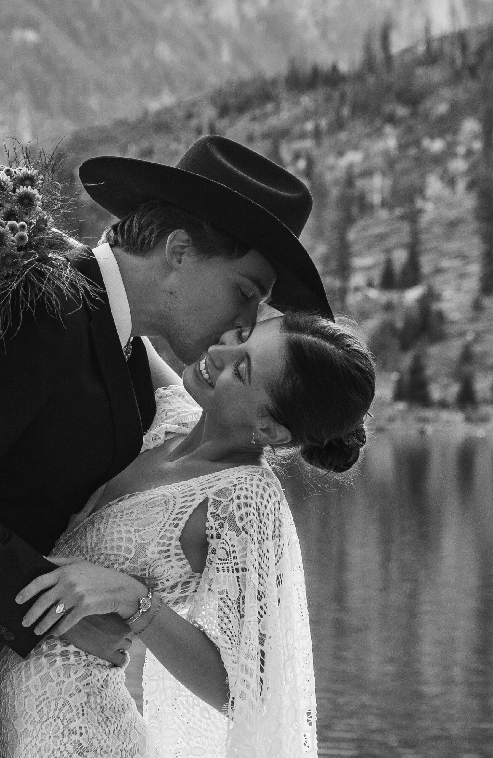 Black and white photo series of a couple in western attire embracing beside a serene lake in Grand Teton National Park.