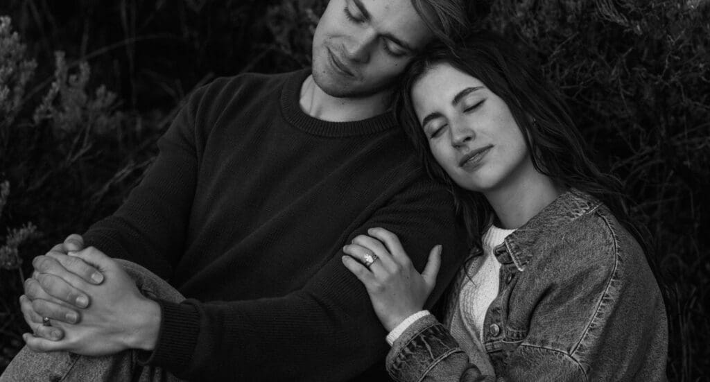 Couple posing together in a scenic meadow at sunset with dramatic clouds and mountain views in Grand Teton National Park.