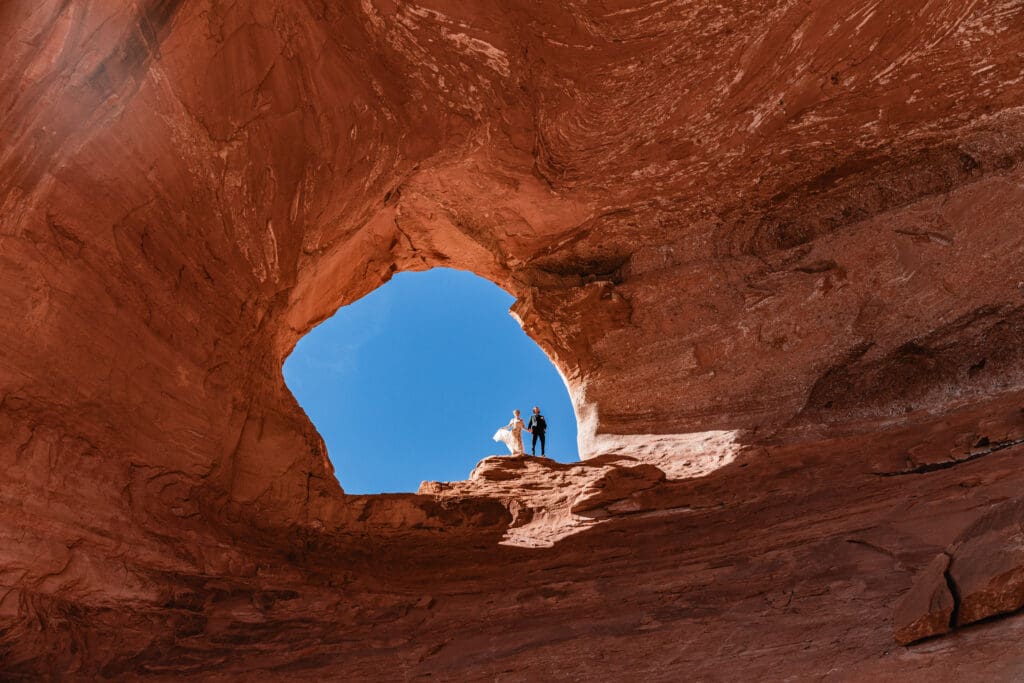 Bride and groom posing in Looking Glass Arch, capturing a romantic elopement moment in Moab’s desert landscape.