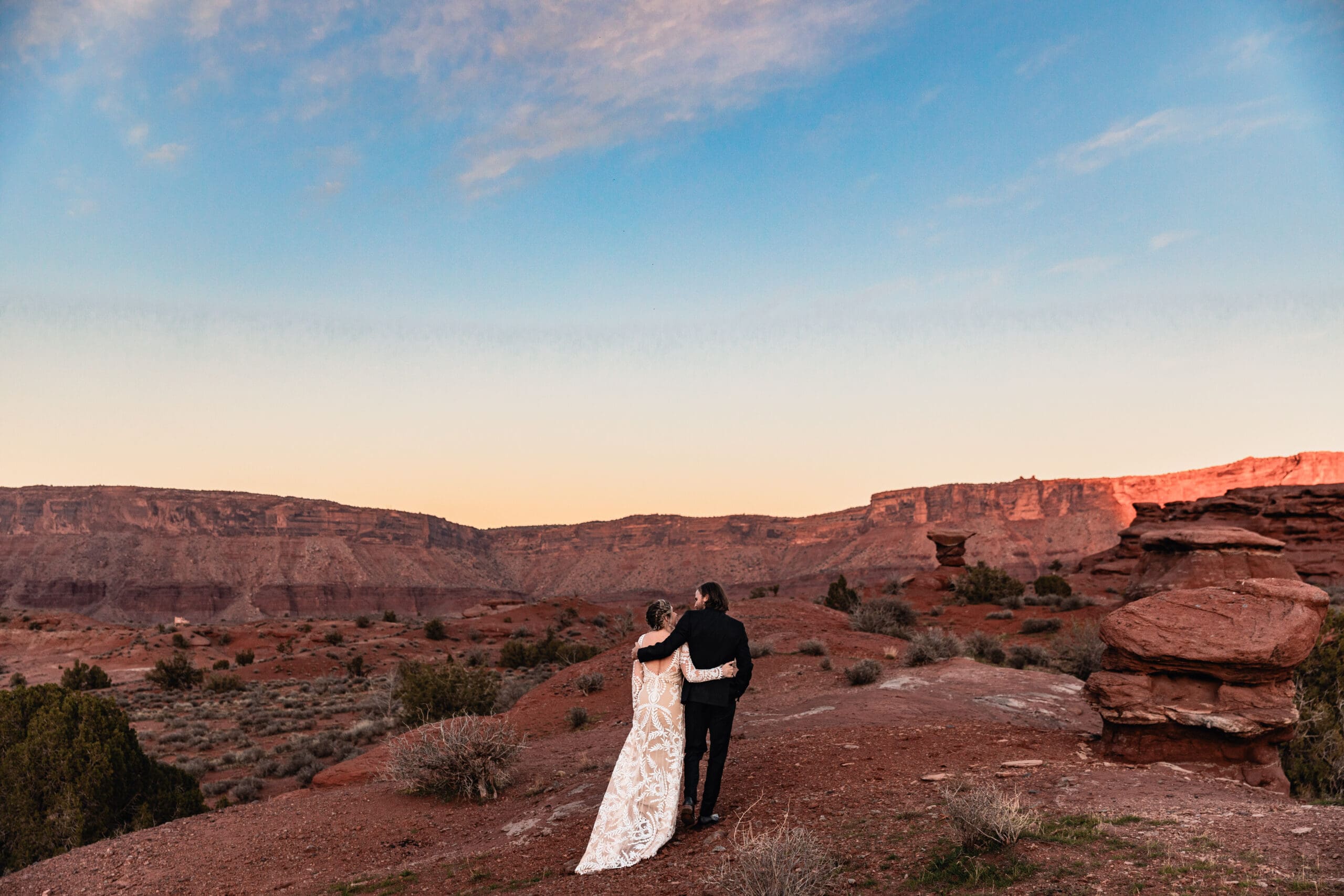 Elopement couple walking arm in arm at sunset in Moab, Utah, celebrating their marriage in the desert landscape.