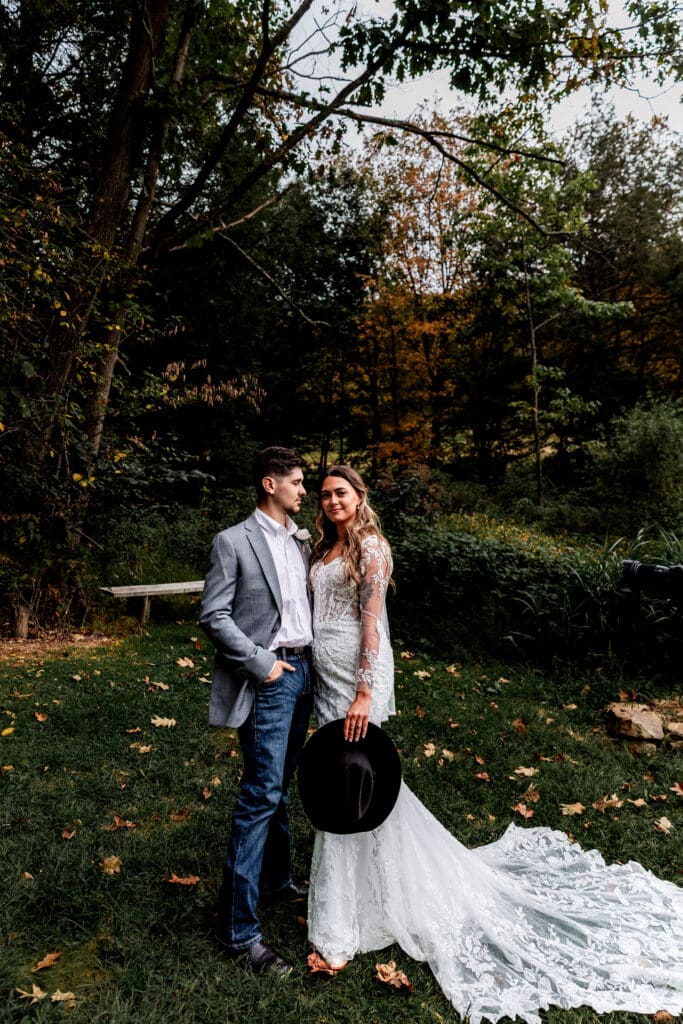 Wedding couple framed by vibrant fall foliage with one partner sitting on a rustic bench at Hinckston Run Farm