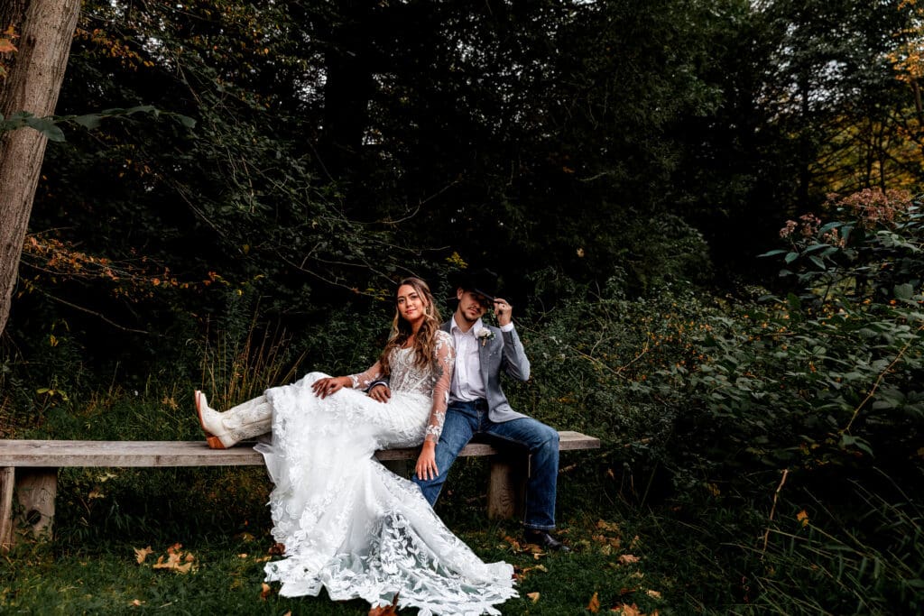 Couple enjoying a quiet wedding portrait moment surrounded by fall leaves with one partner seated on a wooden bench at Hinckston Run Farm