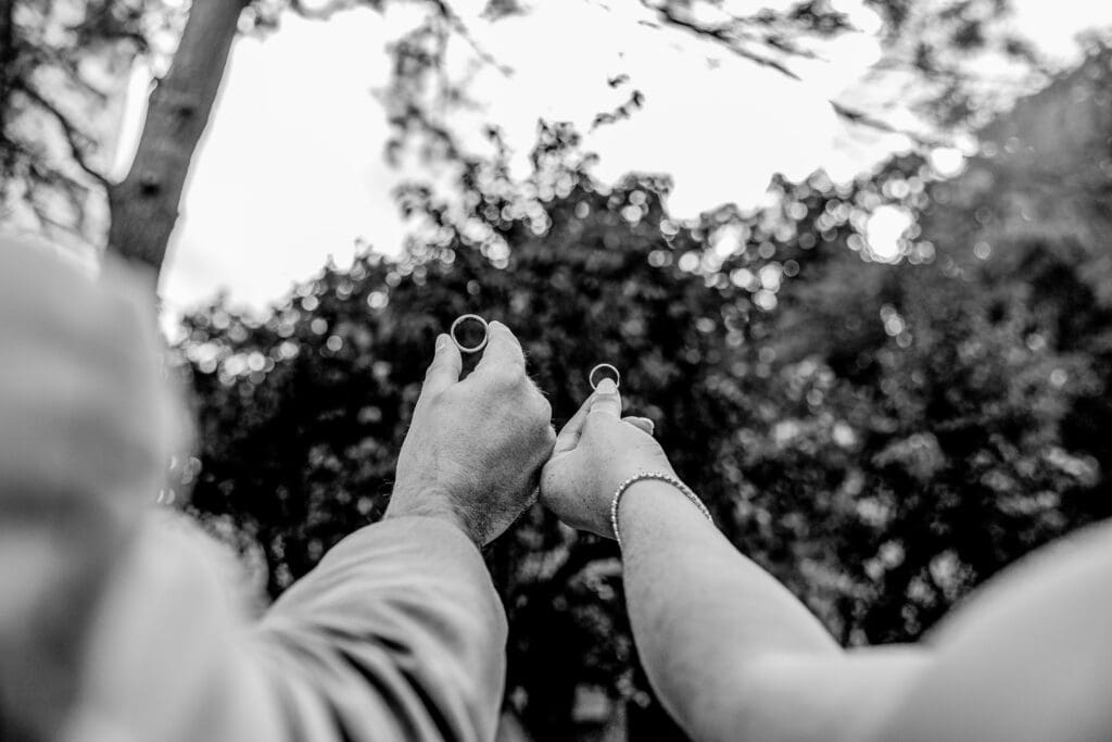 Close up of couple holding wedding bands up in the air at Pittsburgh wedding