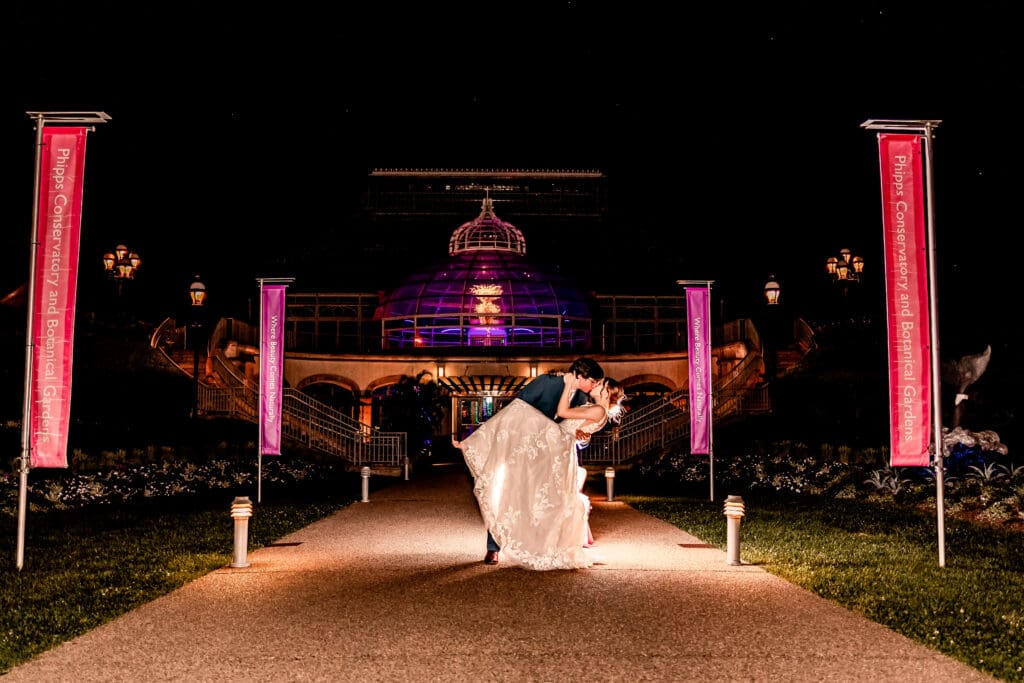 Bride and groom sharing a dip kiss in front of an illuminated Phipps Botanical Gardens at the end of their wedding day