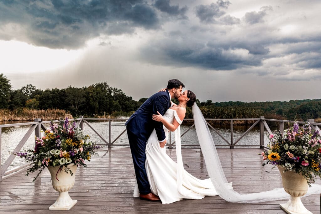 Bride and groom dip kiss beneath dark rain clouds during their Willowbrook wedding in Volant, PA