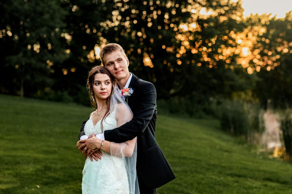 Wedding couple embraces on a hill overlooking a pond at Willowbrook