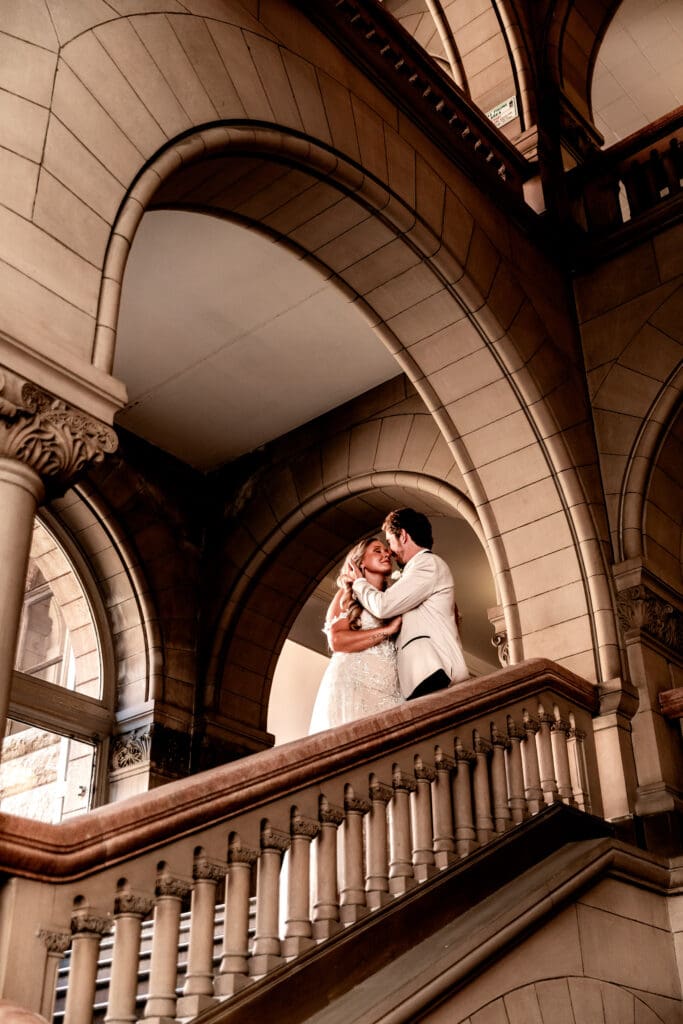 Bride and groom standing on the staircase framed by architectural archways at Allegheny County Courthouse in Pittsburgh