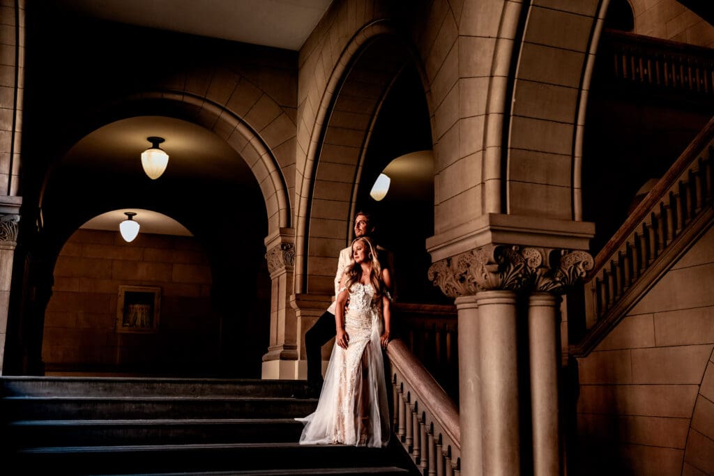Bride and groom standing on the staircase framed by architectural archways at Allegheny County Courthouse in Pittsburgh