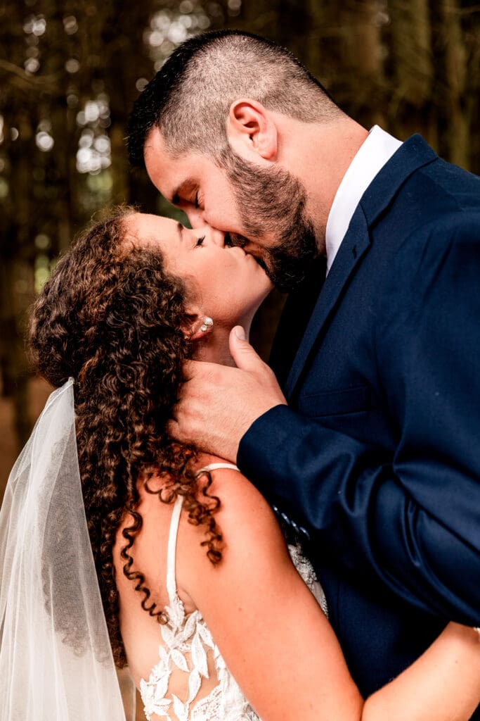 Newlyweds sharing a kiss in the pine tree grove at Sanaview Farm in Somerset, Pennsylvania