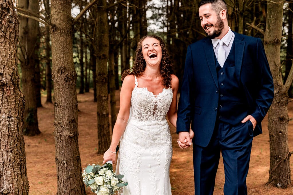 Bride laughing as she embraces her groom among the pine trees at Sanaview Farm wedding in Somerset, Pennsylvania