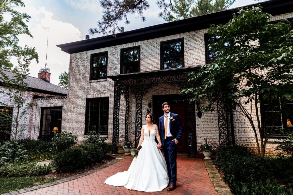 Bride and groom posing on red brick path in front of white brick house with black trim at Succop Nature Park