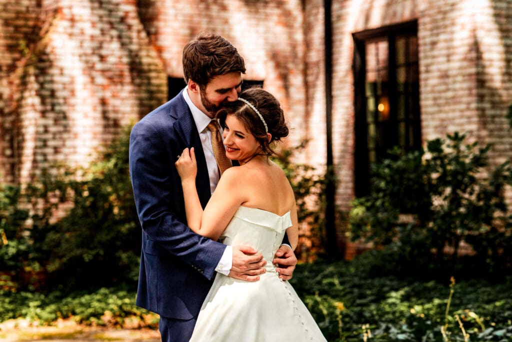 Bride and groom embracing outside rustic brick building with climbing vines at Succop Nature Park