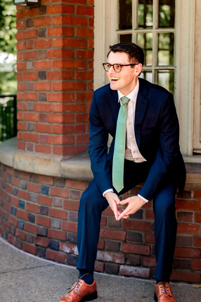 Groom leaning against a wall and smiling at his bride during portraits at Schenley Park Welcome Center