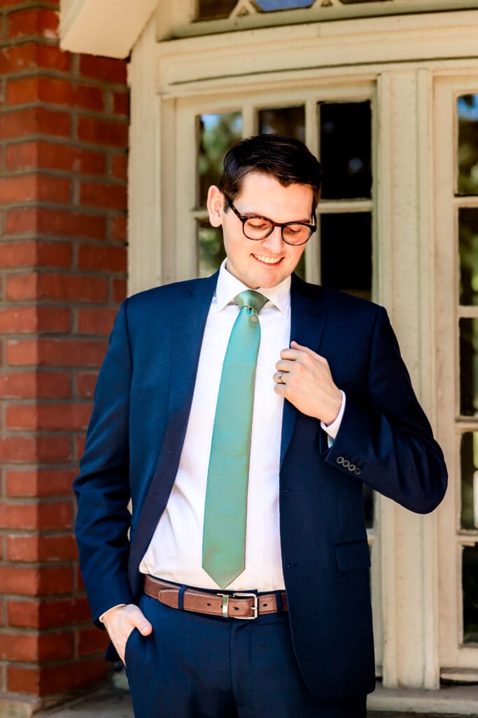 Groom fixing his suit and smiling during wedding portraits at Schenley Park Welcome Center in Oakland