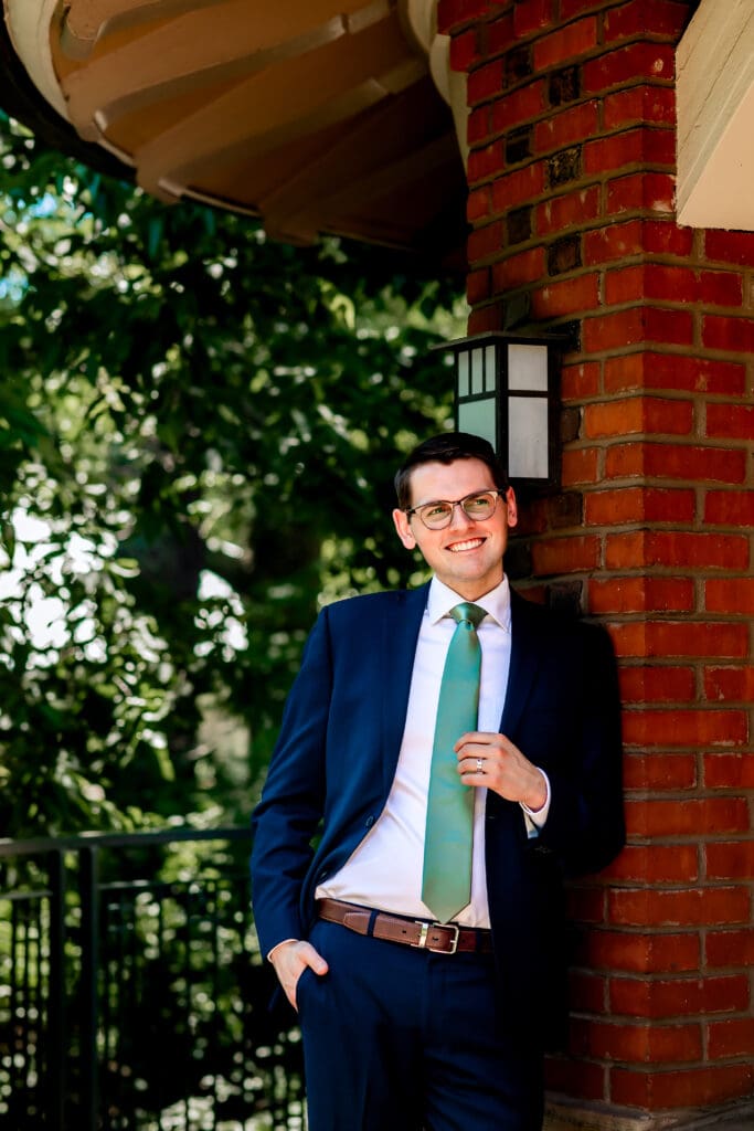 Groom leaning against a wall and laughing during wedding portraits at Schenley Park Welcome Center in Pittsburgh