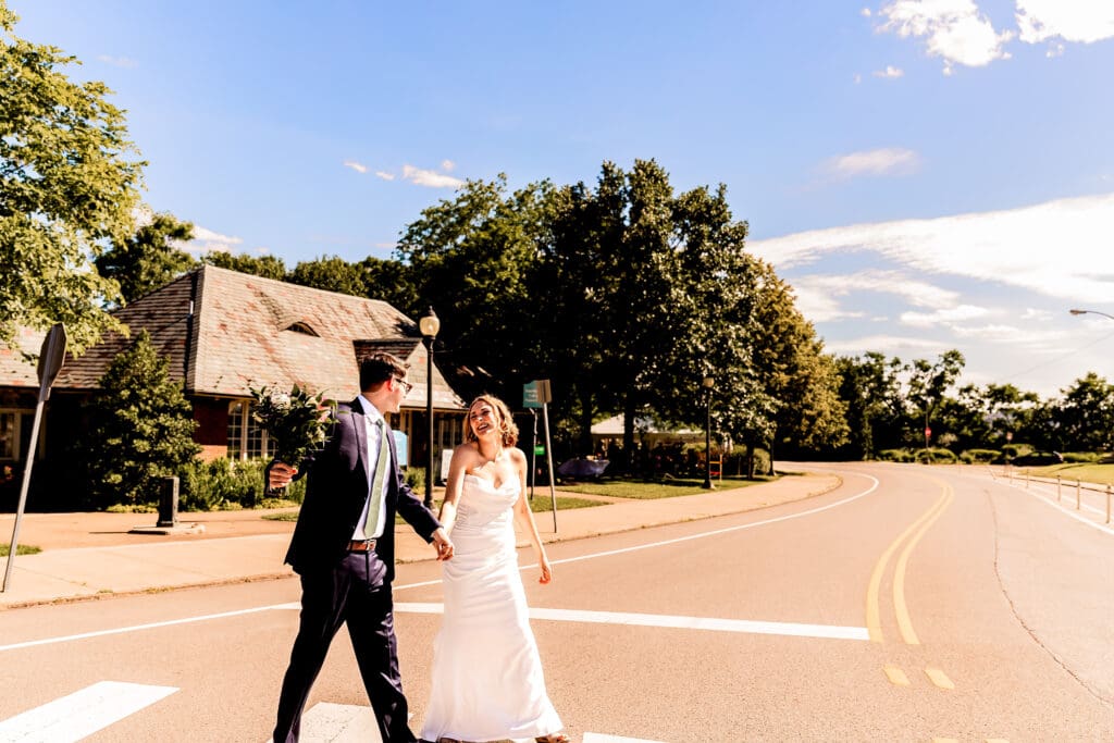 Bride and groom smiling and celebrating in a crosswalk in front of the Schenley Park Welcome Center in Oakland, Pittsburgh