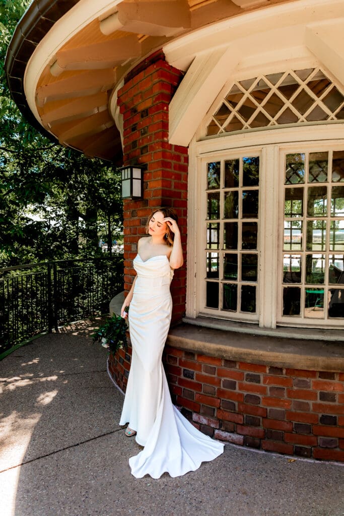 Bride leaning against a wall and brushing hair away from her face during wedding portraits at Schenley Park Welcome Center