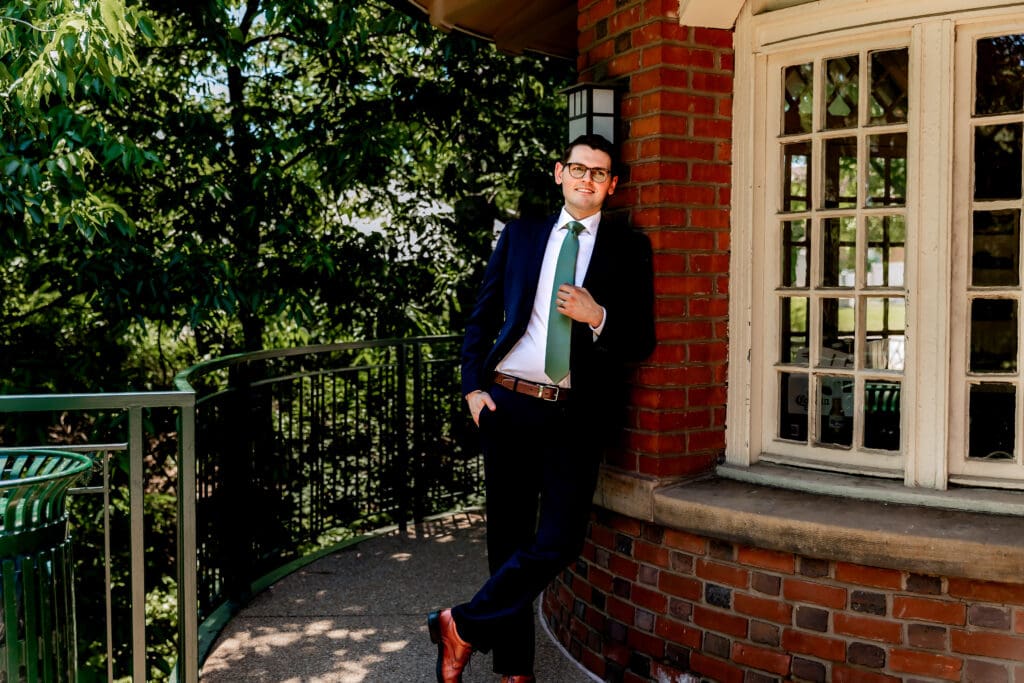 Groom leaning against a wall and smiling at his bride during portraits at Schenley Park Welcome Center