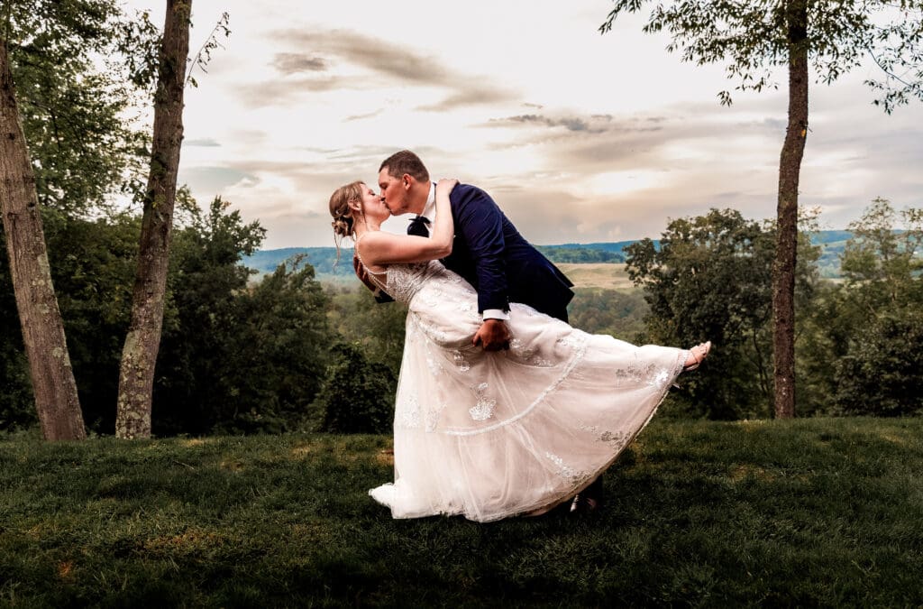 Bride and groom sharing a dip kiss at sunset overlooking The Barn at Ever Thine wedding venue in Butler County, PA