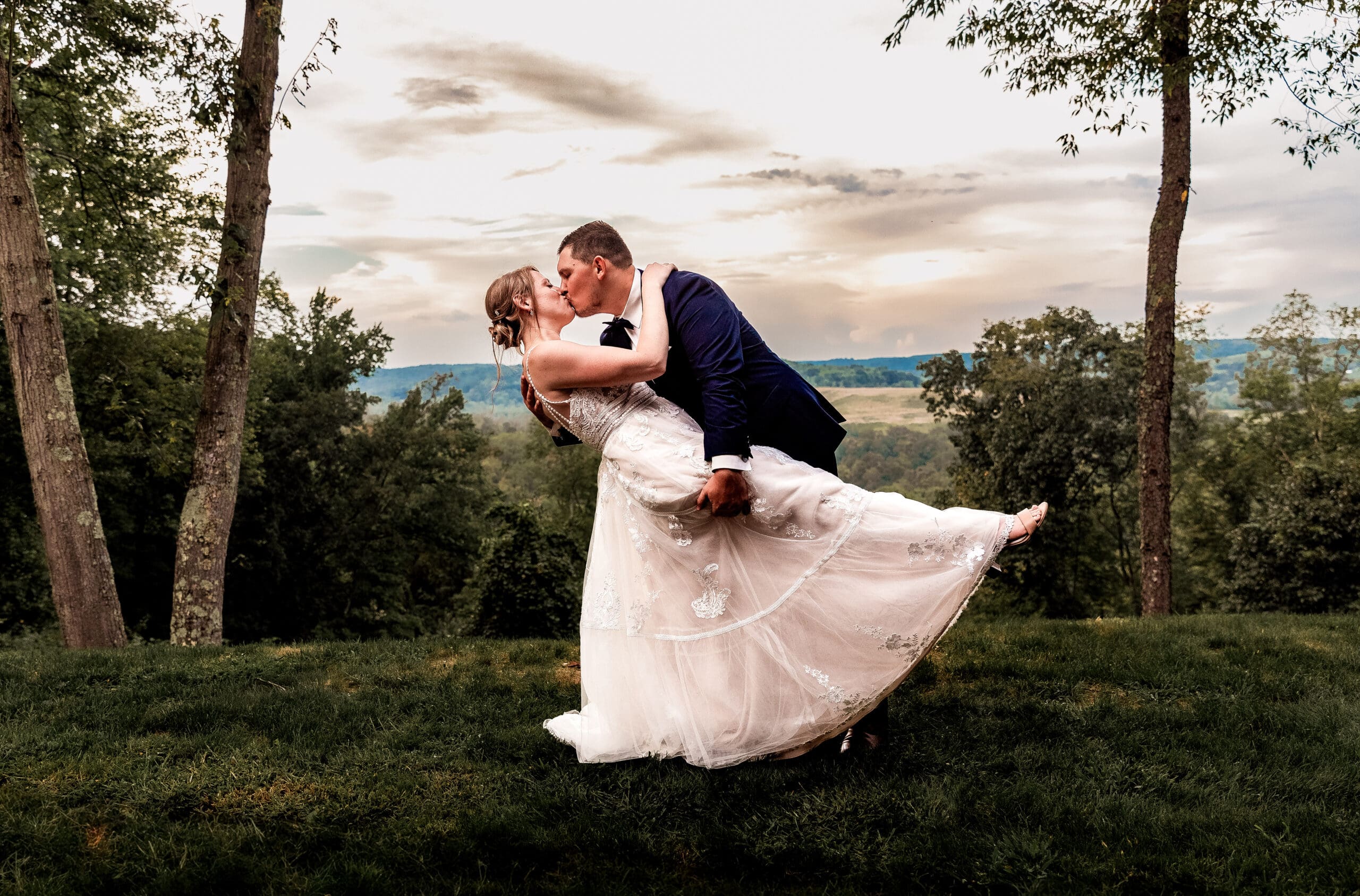 Bride and groom sharing a dip kiss at sunset overlooking The Barn at Ever Thine wedding venue in Butler County, PA