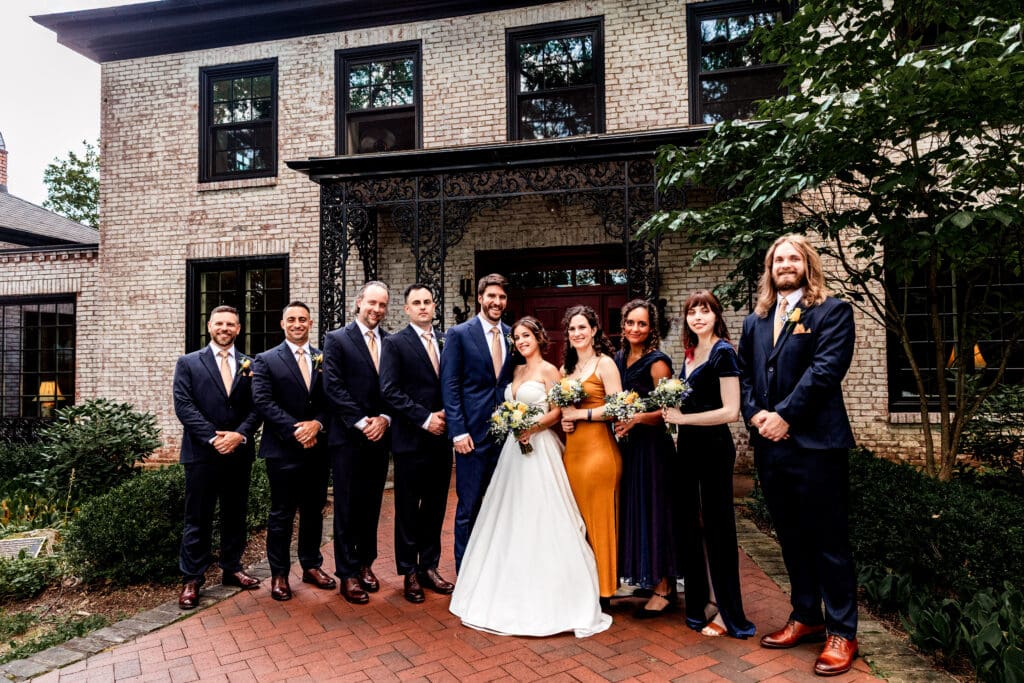 Wedding party standing together for formal portraits outside brick building at Succop Nature Park
