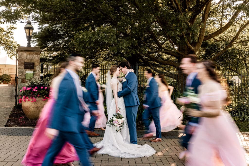 Pittsburgh couple embraces as their wedding party joyfully runs toward them in Phipps Botanical Gardens