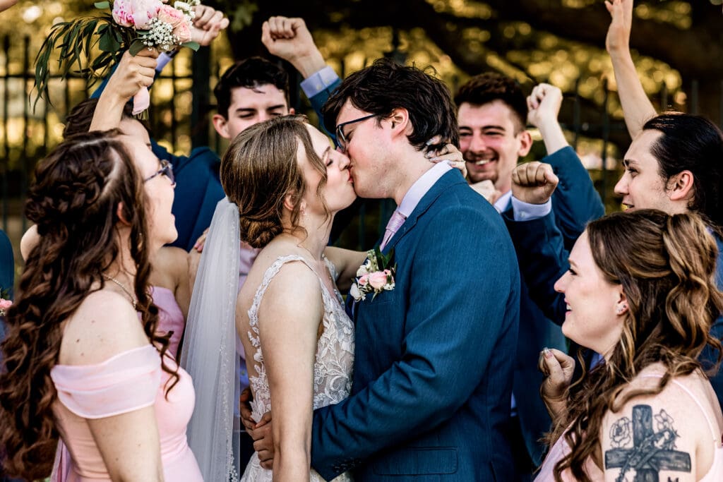 Pittsburgh bride and groom share a kiss while their wedding party cheers around them at Phipps Botanical Gardens