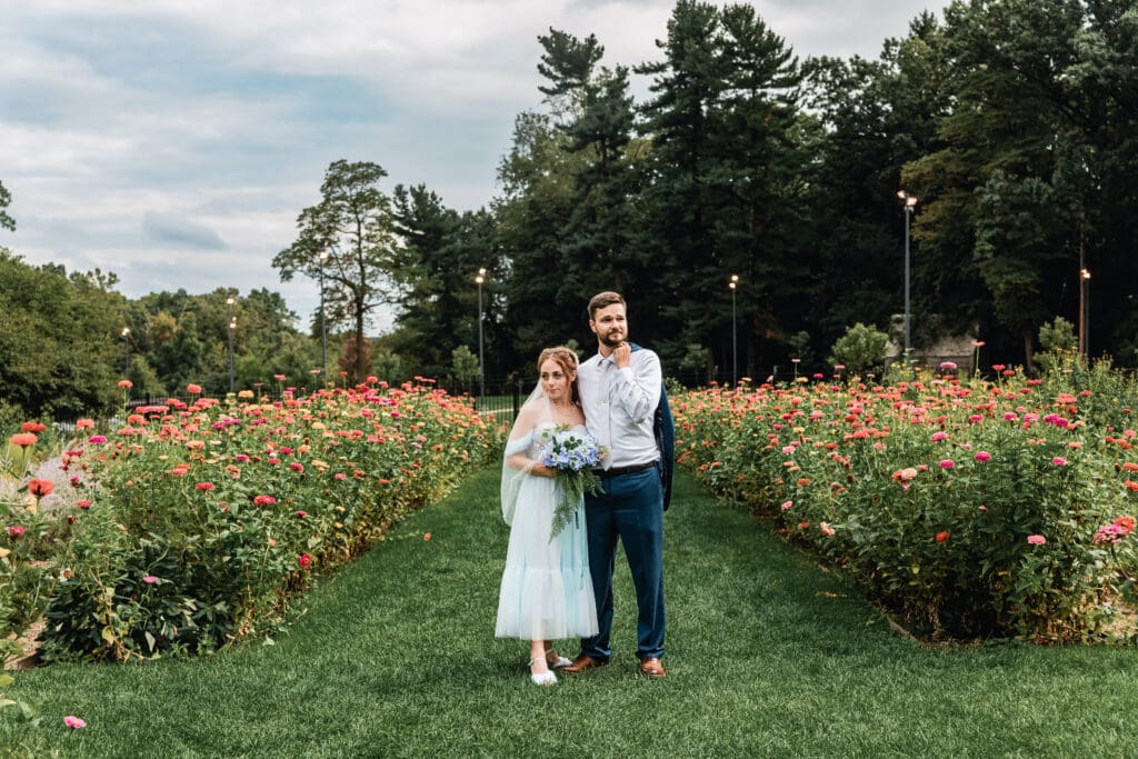Wedding couple stands on a green lawn path between flower gardens during a Hartwood Acres ceremony