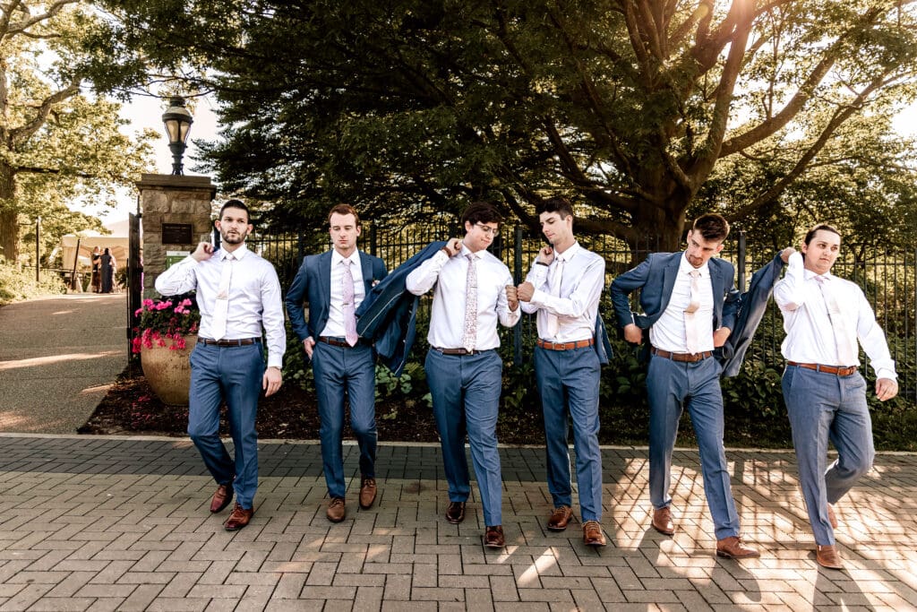 Pittsburgh groom and groomsmen walking toward the camera, fist-bumping and swinging jackets over shoulders during a Phipps Botanical Gardens wedding