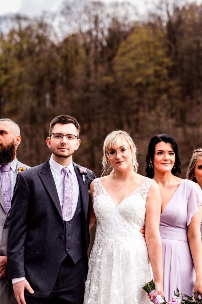 Wedding party in grey and lavender attire posing by a lake near The Fez on a cloudy day