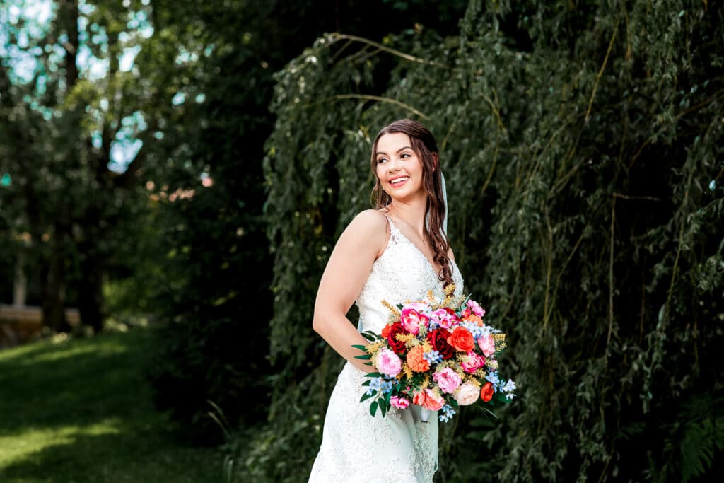 Bride holds a vibrant bouquet beneath a willow tree at Willowbrook