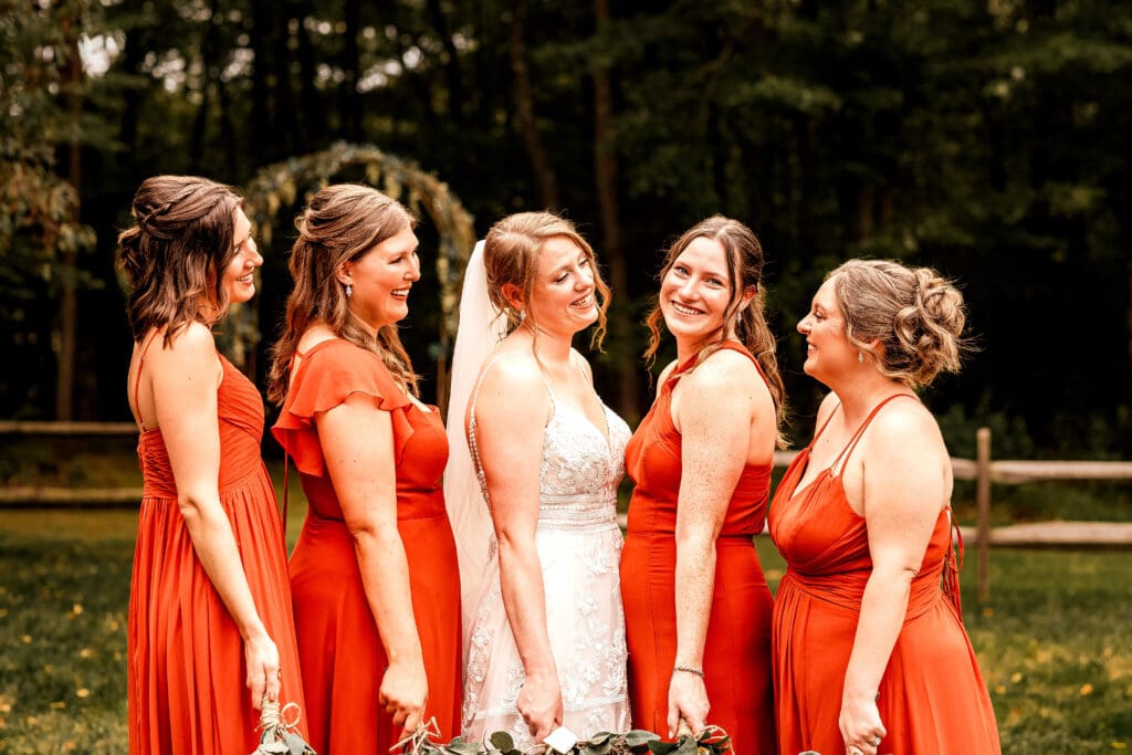 Bridesmaids in tangerine dresses laughing together during wedding portraits at The Barn at Ever Thine in Butler County, PA